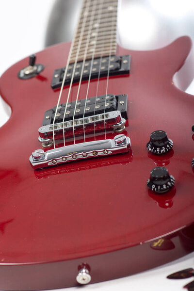 A Close up of a red electric guitar with buttons and strings on a white background