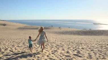 Anne ve kızı Dune du Pyla 'da kumda koşuyorlar.