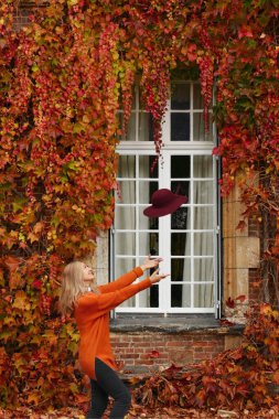 Sonbaharda vahşi üzümlü, turuncu kazaklı bir kadın duvarın yanında.