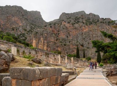 Delphi, Greece. May 2021:   Panoramic view on Temple of Apollo and stoa of Athenians in Delphi against the background of mountains and the sky with clouds in Greece