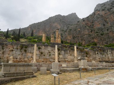 Apollo Tapınağı 'nın panoramik manzarası ve Delphi' deki Atinalıların stoası, Yunanistan 'daki bulutlarla dağların ve gökyüzünün arka planına karşı.