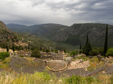 Panoramic view on ancient theater and temple of Apollo with columns in Delphi against the background of mountains and the sky with clouds in Greece
