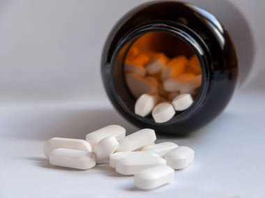 Beyaz ilaç hapları kahverengi bir şişeden etrafa saçılmış.