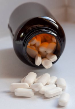 Beyaz ilaç hapları kahverengi bir şişeden etrafa saçılmış.