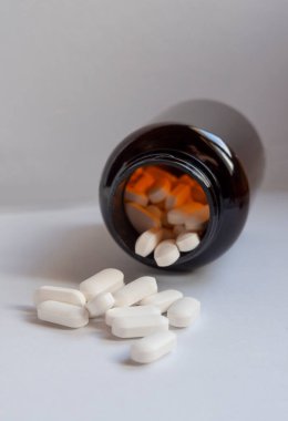 Beyaz ilaç hapları kahverengi bir şişeden etrafa saçılmış.