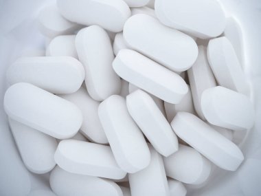 Beyaz ilaç hapları bir şişe konteynırından etrafa saçılmış.