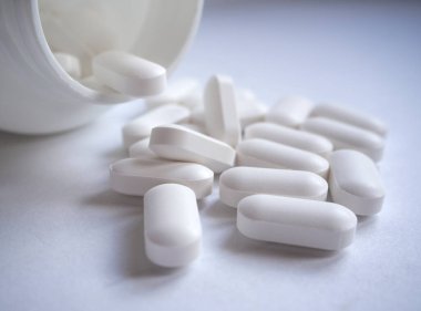 Beyaz ilaç hapları yakın plan beyaz şişe konteynırından yayılmış.