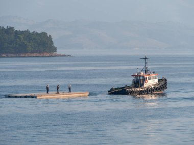 Korfu, Yunanistan. 30 Ekim 2025: Yunanistan 'daki Korfu adasında bir römorkör içinde işçilerle birlikte bir sal sürüklüyor