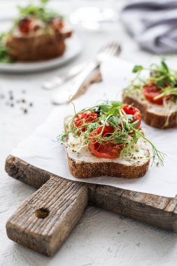 Krem peynirli sağlıklı sandviç, fırında domates ve beyaz arka planda mikro yeşiller. Tahtada domatesli sağlıklı kahvaltı sandviçleri. 