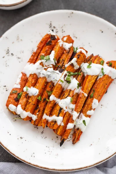 Kızarmış havuç çubukları beyaz bir tabakta. Gri arka planda otlu ve baharatlı fırında havuç. Lezzetli vejetaryen yemeği. Sağlıklı kök sebze kavramı