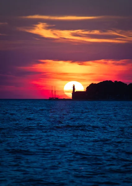 Sailboat and lighthouse on dramatic sunset — Stock Photo, Image