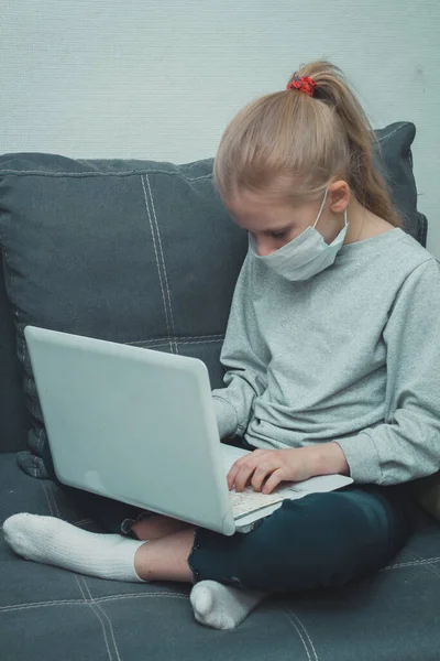 Sevimli küçük kız kanepede oturuyor ve karantinadaki bir laptopta video görüşmesi yapıyor.
