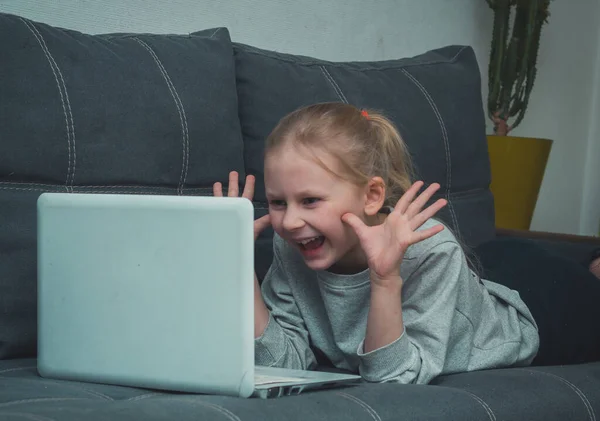 Feliz sorrindo menina deitada no sofá e faz uma chamada de vídeo em um laptop em quarentena — Fotografia de Stock