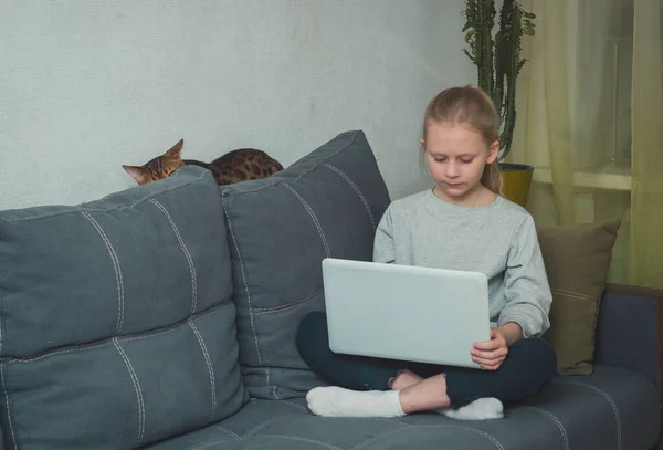 Liseli kız oturma odasında kanepede oturuyor ve dizüstü bilgisayarını kucağında tutuyor. Çocuk internet bağımlılığı konsepti.