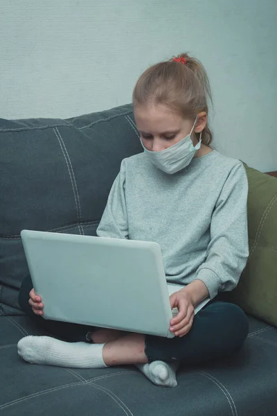 Maskeli kız karantinada dizüstü bilgisayardan video dersleri izliyor.