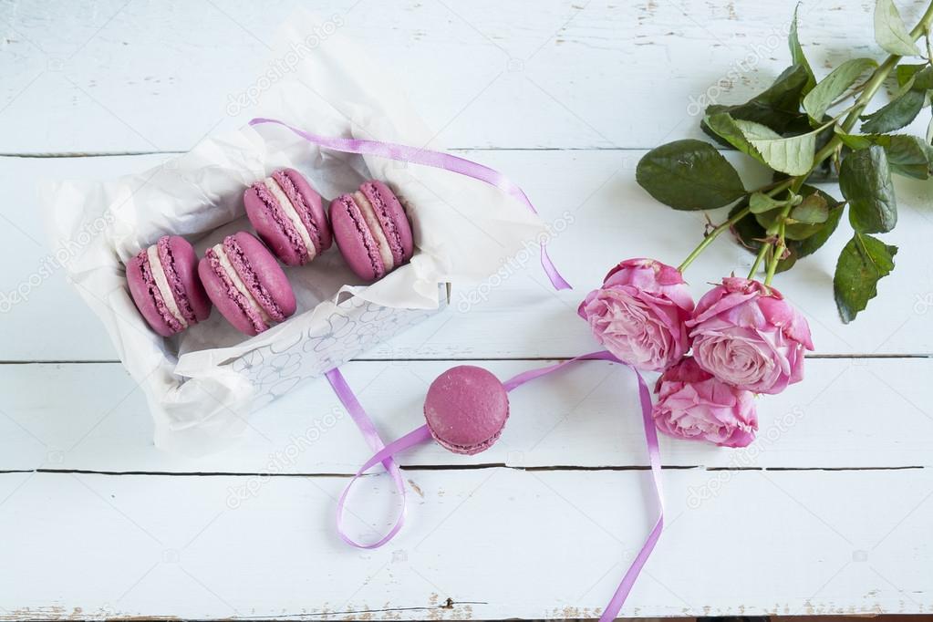 Sweet crimson french macaroons with box and roses on light dyed wooden background