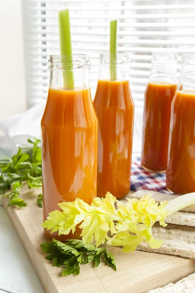 Natural and fresh carrot juice in small bottles with fresh celery and plain rye cakes, galette rye on light background