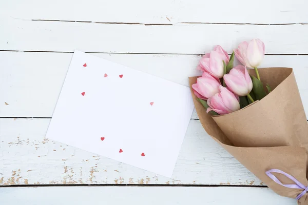 Güzel bir beyaz zarf ve pembe şeker kalpler hafif ahşap zemin üzerine yanında Pembe Lale buketi