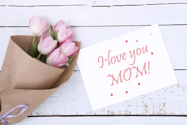 Beautiful bouquet of pink tulips next to a white envelope and pink sugar hearts on light wooden background — Stock Photo, Image