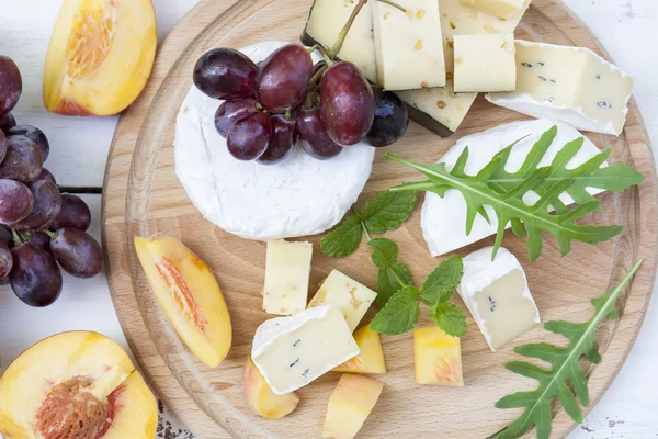 Diversi deliziosi formaggi e frutta su tavola rotonda in legno — Foto Stock