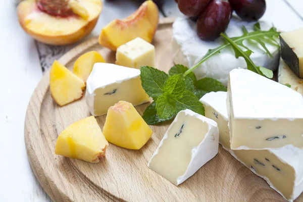 Diversi deliziosi formaggi e frutta su tavola rotonda in legno — Foto Stock