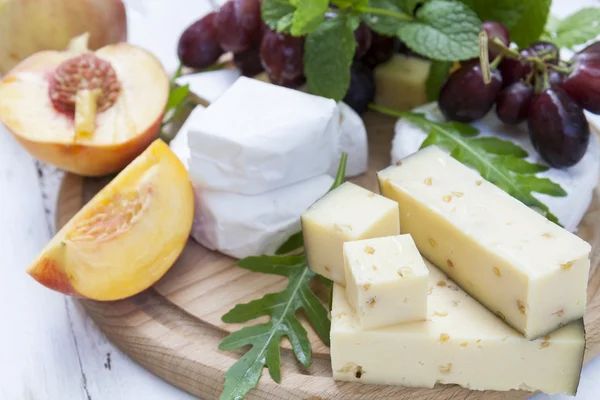 Diversi deliziosi formaggi e frutta su tavola rotonda in legno — Foto Stock