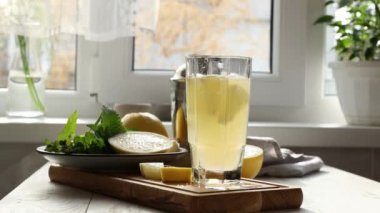 Güneşli sonbaharda, pencerenin yanındaki beyaz masanın camına greyfurt cini ve tonik kokteyle buz koyan kadın. Seçici odaklanma, alanın yüzeysel derinliği. Alkol ya da detoks içeceği..