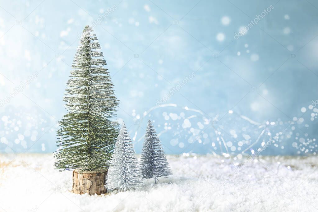 Christmas or winter composition. Little souvenir Christmas trees on soft snow on blue background. Christmas, winter, new year concept.