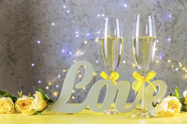 Sarı kurdeleli iki şampanya bardağı aşk mektupları ve güllerle dolu masada duruyor. Yüzeyin derinliği, şenlik sofrası, Aziz Valentine ya da düğün tebrik kartı.