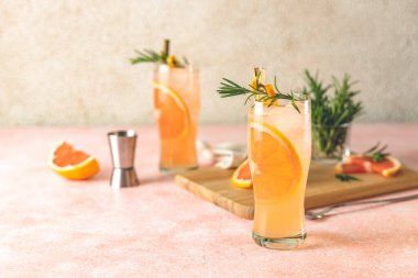 İki kadeh Paloma kokteyli, tekila taze greyfurt suyu ve biberiye. İçindekiler ve bar aletleriyle çevrili. Açık pembe beton yüzey.