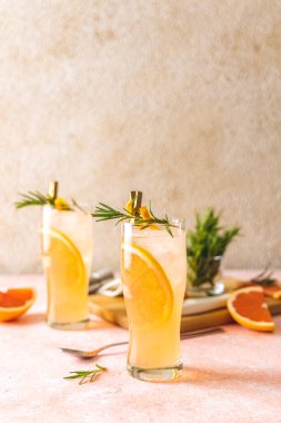 İki bardak Paloma kokteyli, tekila taze greyfurt suyu ve biberiye. Açık pembe beton yüzey.