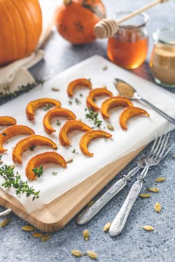 Gri masanın üzerinde tahta bir tahtanın üzerinde kekik dilimlenmiş mini balkabağı dilimleri. Mevsimlik vejetaryen yemek tarifi.