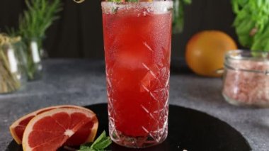 Pembe Greyfurt Mezcal Paloma Kokteyli. Su damlalı viski bardağı boyunca hareket eden bir kamera. Yaklaş, alanın sığ derinliği.