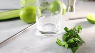 Mojito kokteyli ya da nane, salatalık ve kireç karışımını gri beton yüzey arka planında viski bardağında hazırlıyorum. Kamera cam boyunca hareket ediyor.