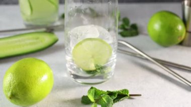 Mojito kokteyli ya da nane, salatalık ve kireç karışımını gri beton yüzey arka planında viski bardağında hazırlıyorum. Kamera cam boyunca hareket ediyor.
