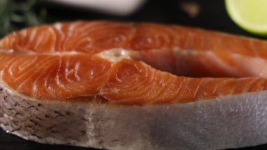 Tahtada çiğ somon bifteği ve tuz, biber, limon, karanfil ve biberiye. Somon balığı pişirmek, deniz mahsulleri. Sağlıklı gıda konsepti. Somon ve baharatlar, daire şeklinde dönüyorlar. Yakın plan.