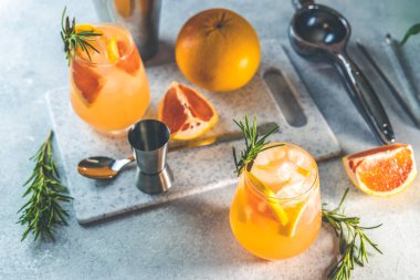 İki bardak soğuk limonata taze greyfurt suyu, alkol ve buz küpleri dilimlenmiş narenciye ve dal biberiyesi, açık gri beton yüzey.