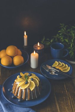 Böğürtlenli turuncu kek. Etrafı meyveler, mumlar, bitkiler ve ahşap arka planda kesiciler ile çevrili. Lezzetli bayramlar akşam yemeği zamanı.