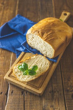 Bir somun taze ekmek fesleğen ve ahşap tahta üzerinde ekmek dilimleri ile rustik ahşap masa arka planında. Seçici odaklanma. Sığ alan derinliği.