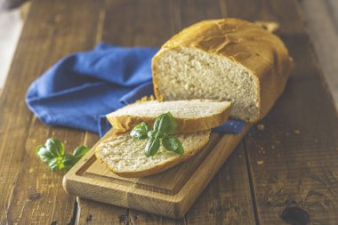 Bir somun taze ekmek fesleğen ve ahşap tahta üzerinde ekmek dilimleri ile rustik ahşap masa arka planında. Seçici odaklanma. Sığ alan derinliği.