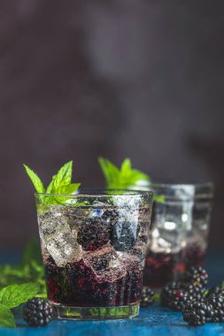 Böğürtlenli soğuk yaz meyveli içecek. Yaz içeceğini şuruplu, böğürtlenli ve buzlu koyu mavi beton arka planda tazeleyici