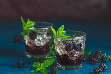 Böğürtlenli soğuk yaz meyveli içecek. Yaz içeceğini şuruplu, böğürtlenli ve buzlu koyu mavi beton arka planda tazeleyici