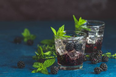 Böğürtlenli soğuk yaz meyveli içecek. Yaz içeceğini şuruplu, böğürtlenli ve buzlu koyu mavi beton arka planda tazeleyici