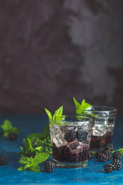 Böğürtlenli soğuk yaz meyveli içecek. Yaz içeceğini şuruplu, böğürtlenli ve buzlu koyu mavi beton arka planda tazeleyici