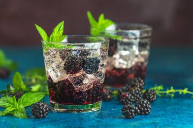 Böğürtlenli soğuk yaz meyveli içecek. Yaz içeceğini şuruplu, böğürtlenli ve buzlu koyu mavi beton arka planda tazeleyici