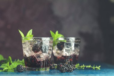 Böğürtlenli soğuk yaz meyveli içecek. Yaz içeceğini şuruplu, böğürtlenli ve buzlu koyu mavi beton arka planda tazeleyici