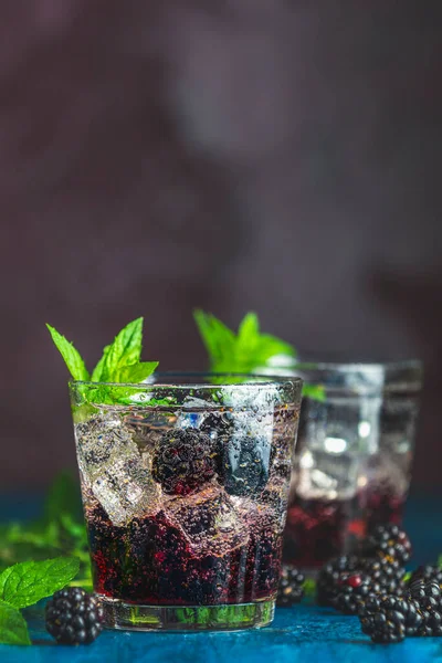 Böğürtlenli soğuk yaz meyveli içecek. Yaz içeceğini şuruplu, böğürtlenli ve buzlu koyu mavi beton arka planda tazeleyici