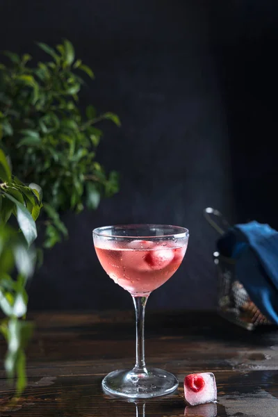 精美的粉红色玫瑰香槟 冰块里有冰冻的覆盆子 水滴在深色的木制桌子上 密闭在田野浅浅的深处 — 图库照片