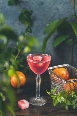 Koyu ahşap masa yüzeyinde buzlu ahududu ve donmuş ahududu içeren zarif kadehler yeşil bitkiler, buz ve taze kan portakalı sepette..