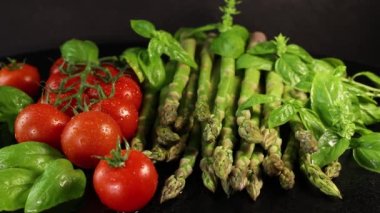 Lezzetli taze vişneli domates dalıyla su damlaları, yeşil fesleğen yaprakları ve yeşil çiğ kuşkonmaz siyah arkaplanı açıyor.